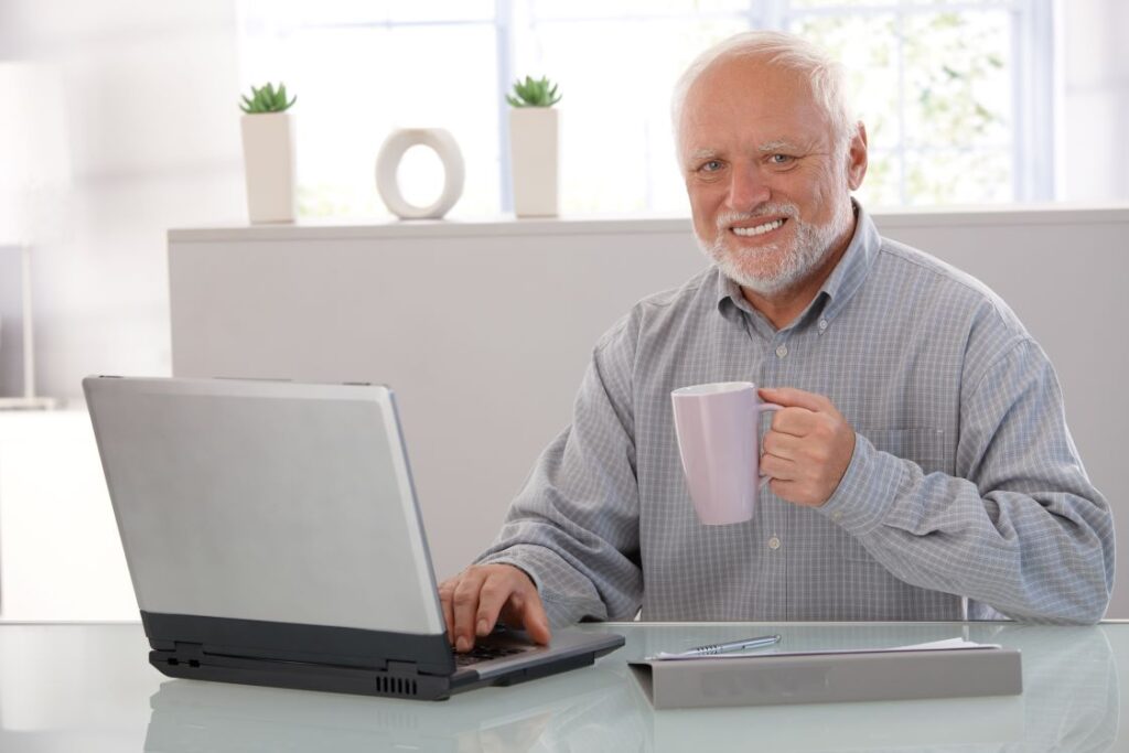 An older man sitting in front of a computer and holding a mug.